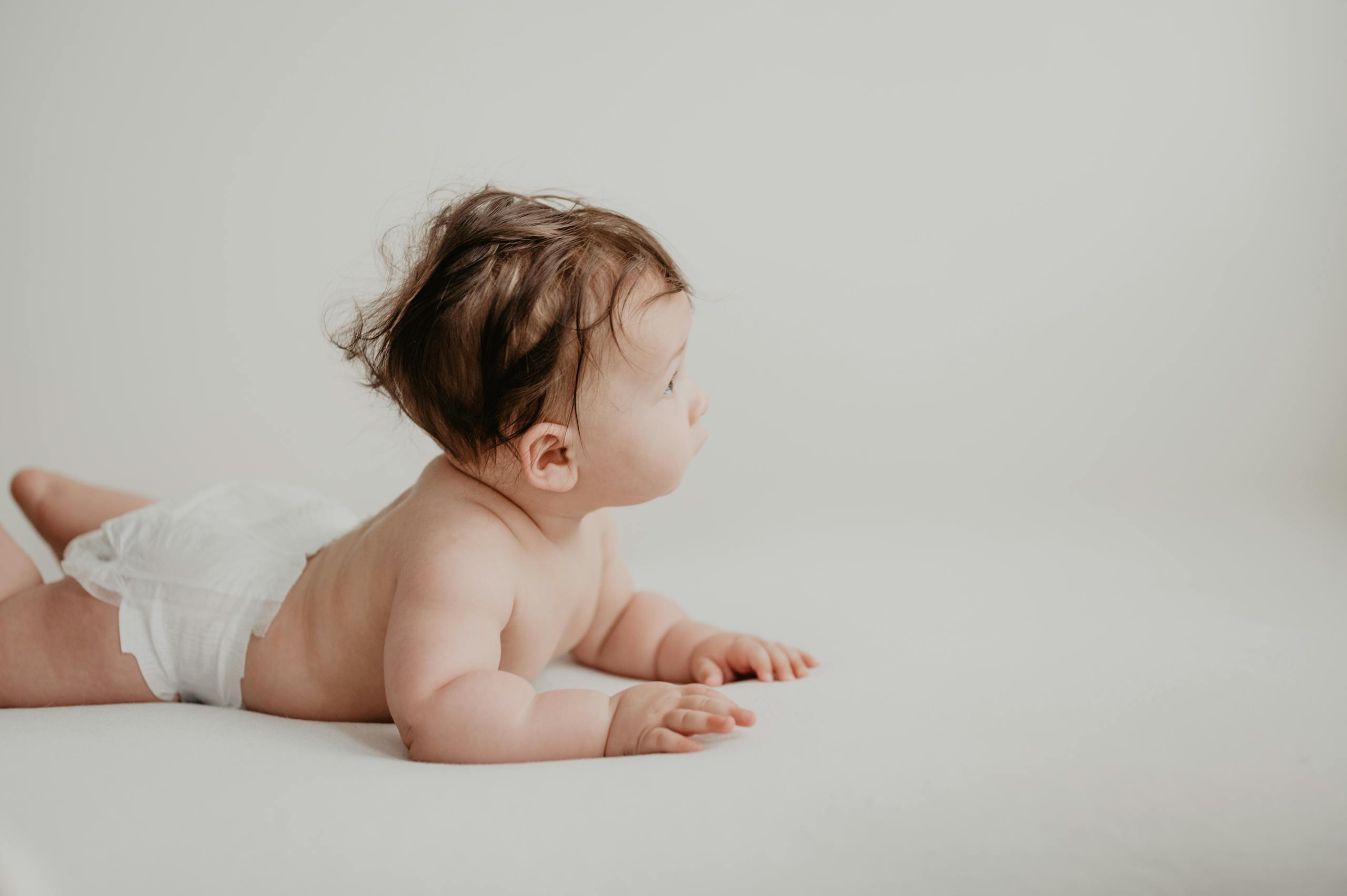 Cute baby in a diaper lying on a white surface with a neutral background.